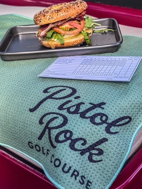 A made-to-order sandwich on an everything bagel next to a Pistol Rock scorecard